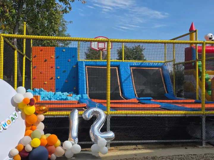 Arena de trambuline cu plasă de protecție, perete de cățărare portocaliu și albastru și piscină cu bile